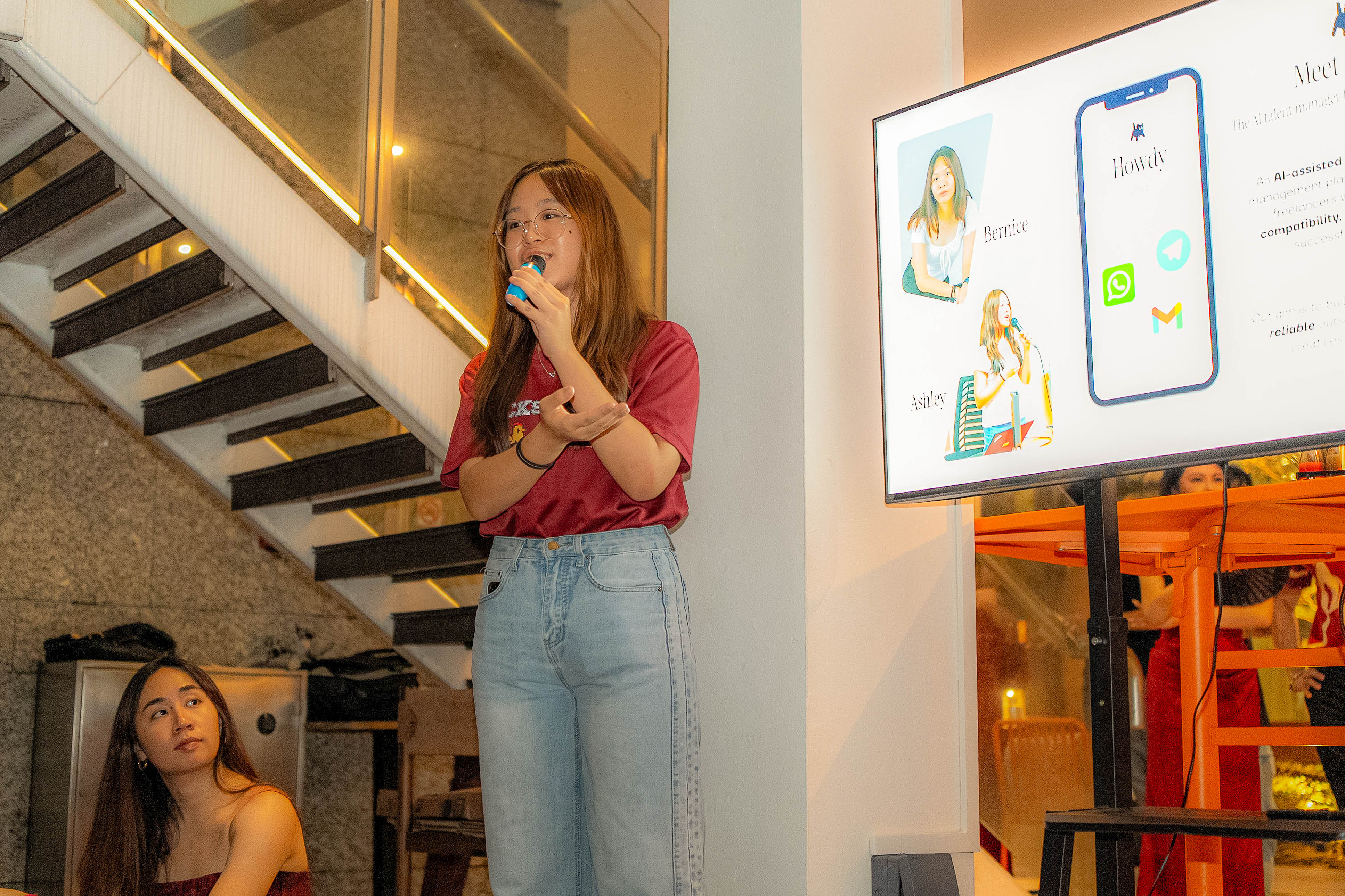 Ashley speaking into the mic, with the Meet Howdy slide behind